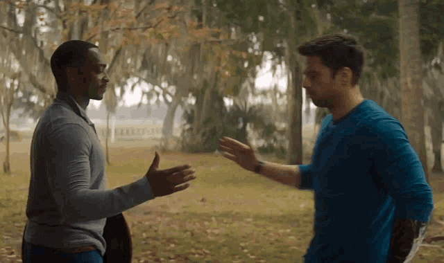 a man in a blue shirt is shaking hands with another man in a grey shirt