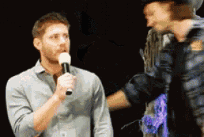 a man is talking into a microphone while another man looks on