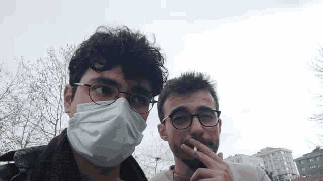 a man wearing glasses and a mask stands next to another man