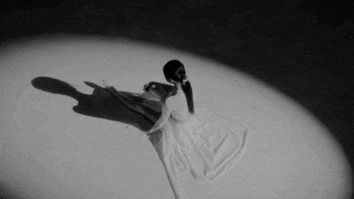 a black and white photo of a woman in a white dress dancing on a stage .