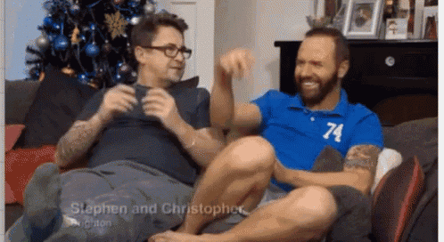 two men are sitting on a couch with one wearing a blue shirt with the number 74 on it