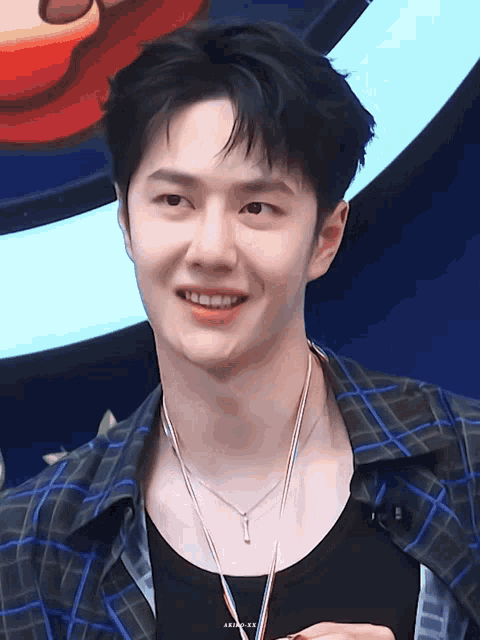 a close up of a young man wearing a plaid shirt and a necklace with the letters aria on it