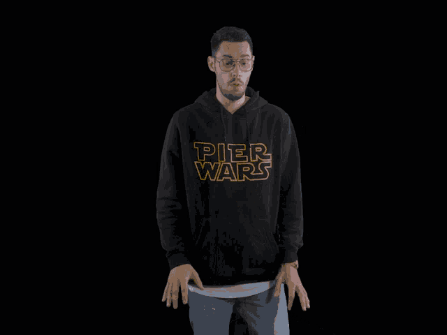 a man wearing a pier wars hoodie is standing in front of a black background