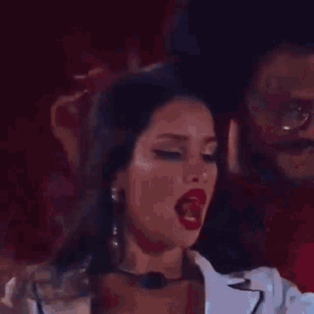 a man and a woman are sitting next to each other and the woman is wearing red lipstick and a microphone .