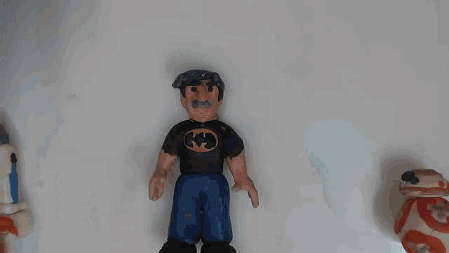 a man wearing a batman shirt stands next to a r2d2 and a bb-8