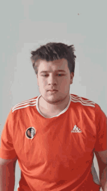 a man wearing a red adidas shirt looks down