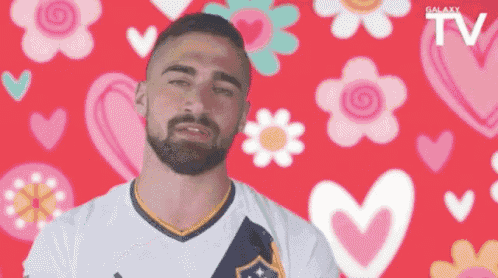 a man with a beard is standing in front of a red background with hearts and flowers