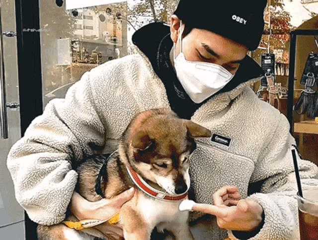 a man wearing a mask and an obey hat holds a dog