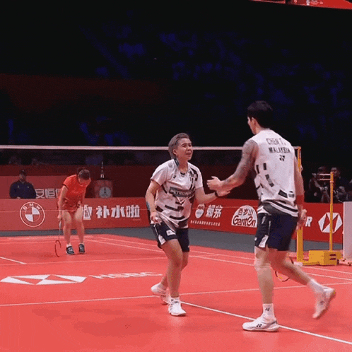 a man in a malaysia jersey shakes hands with a woman on a badminton court
