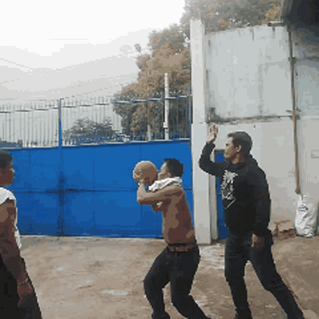 a group of men are playing a game of basketball in front of a blue fence