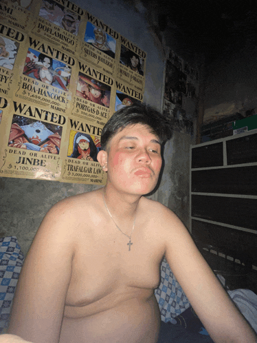 a shirtless man sitting in front of a wall with wanted posters on it