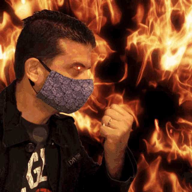 a man wearing a purple face mask stands in front of fire