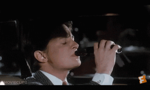 a man in a suit is drinking a beer from a bottle while smoking a cigarette .