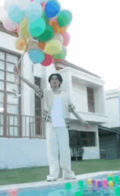 a man is holding a bunch of colorful balloons in front of a house .