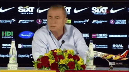 a man sitting at a table with a bunch of flowers in front of a sixt logo