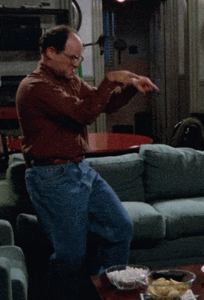 a man in a brown shirt and blue jeans is dancing in front of a couch