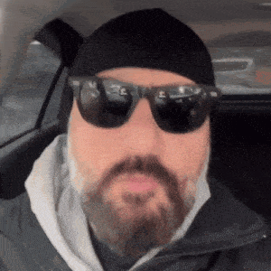 a man with a beard wears sunglasses and a black hat