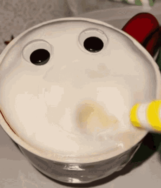a white bowl with googly eyes and a yellow and white stripe