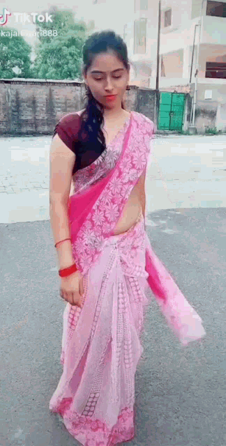 a woman in a pink saree is standing on the side of the road .
