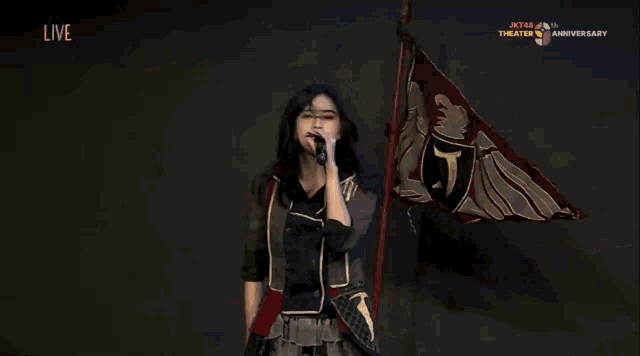 a woman singing into a microphone in front of a flag that says theater