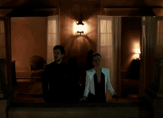 a man and a woman standing in a dark room with a light on the wall