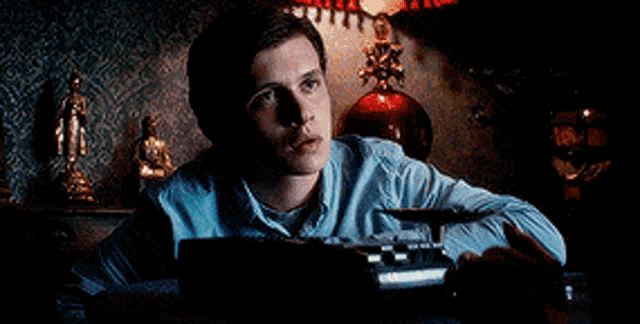 a man in a blue shirt is sitting at a desk with a typewriter in front of him .