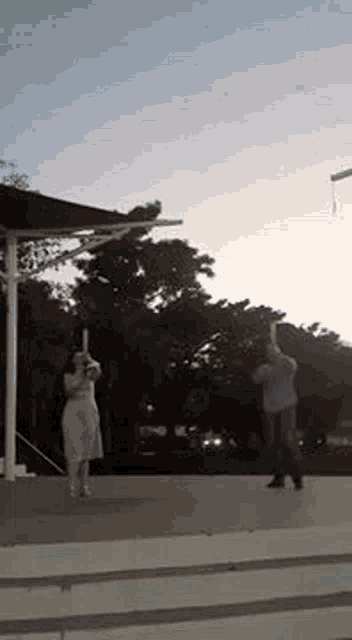 a woman is taking a picture of a man holding a stick in a park .