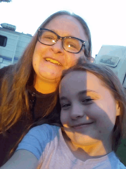 a woman and a girl are posing for a picture in front of a rv that says ' rv ' on it
