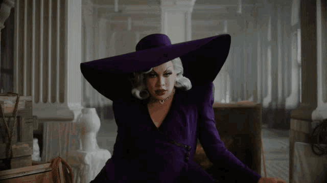 a drag queen wearing a purple hat and a purple dress