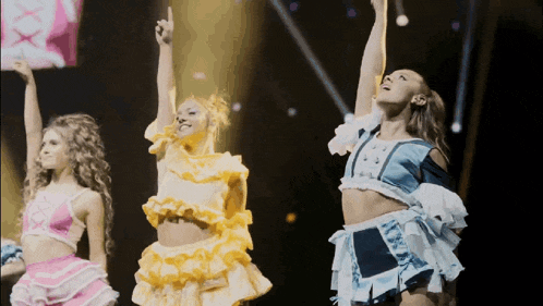 three women are dancing on a stage with their arms up