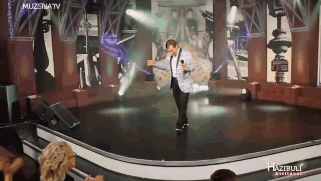 a man in a suit is singing on a stage in front of a crowd that is applauding him
