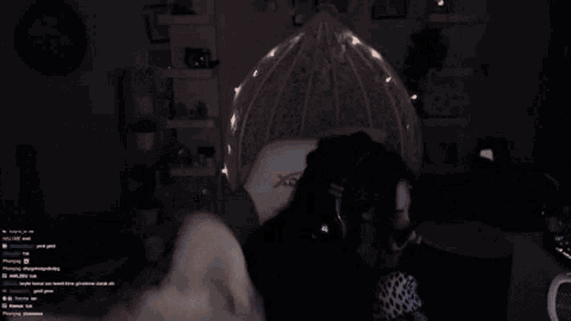 a white cat is looking at the camera in a dark room with a person in the background