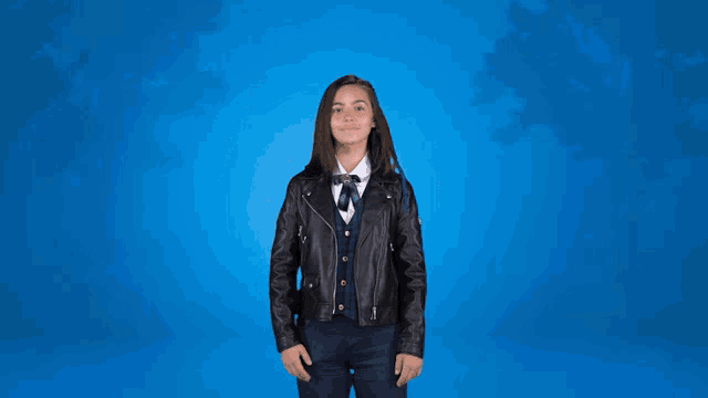 a girl wearing a leather jacket and plaid vest is waving her hands