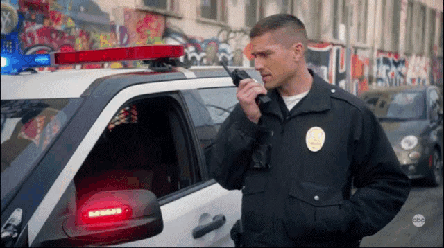 a police officer is talking on a walkie talkie next to a police car