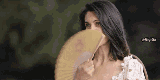 a woman holding a fan in front of her face with the hashtag gigigx below her