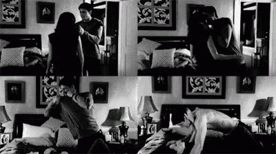 a black and white photo of a man and a woman kissing in a bedroom .