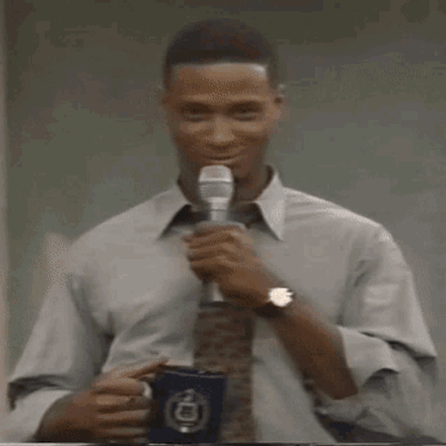 a man in a tie is holding a microphone and a cup