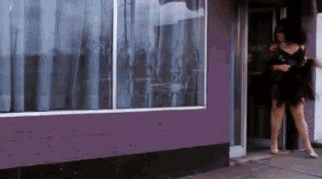 a woman in a black dress is standing in front of a purple building with a window .