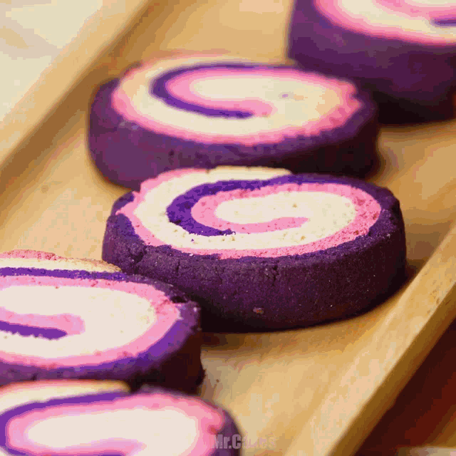 purple and pink cookies on a wooden tray with the words mr.cakes on the bottom