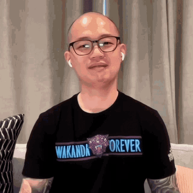 a bald man wearing glasses and a black t-shirt that says wakanda forever