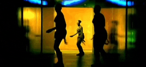a woman is dancing in a dark room with a neon sign behind her .