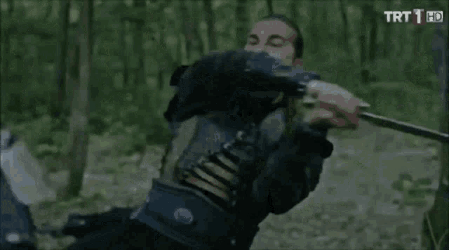 a man in armor is holding a sword and another man is holding a sword in the woods .