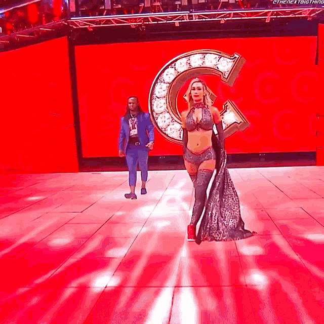 a woman is walking on a stage in front of a large c