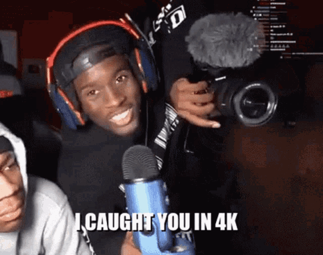 a man wearing headphones is holding a camera and a microphone and says i caught you in 4k