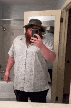 a man with a beard is taking a selfie in front of a mirror