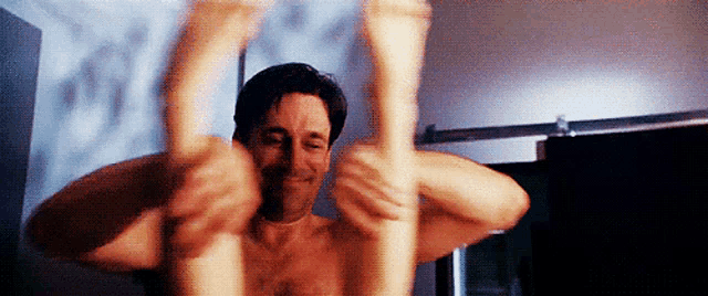 a man without a shirt is holding a woman 's legs in his arms .