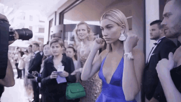 a woman in a blue dress with a plunging neckline is standing in front of a crowd of people .