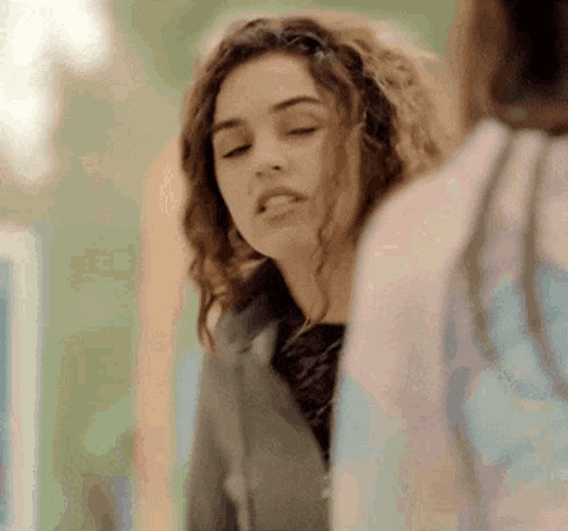 a girl with curly hair is looking at herself in a mirror .