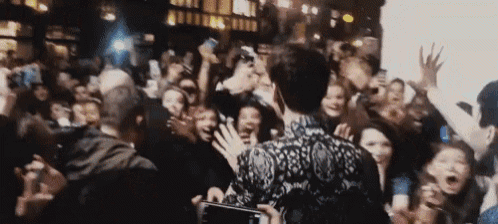 a man is standing in front of a crowd of people holding up their hands .