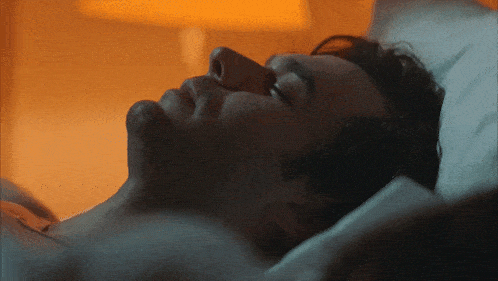 a man laying in bed with his eyes closed and a lamp in the background